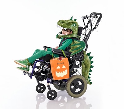 A child in an electric wheelchair wearing an adaptive green t-rex dino costume in an article about h...
