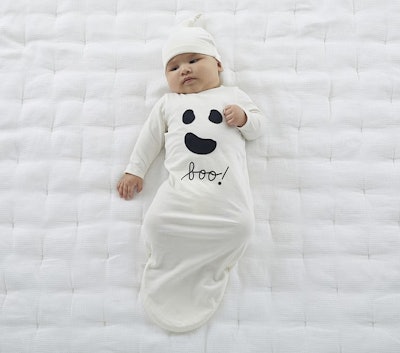 A baby wearing a swaddle with a ghost face on it that says, "boo" in script underneath for an articl...