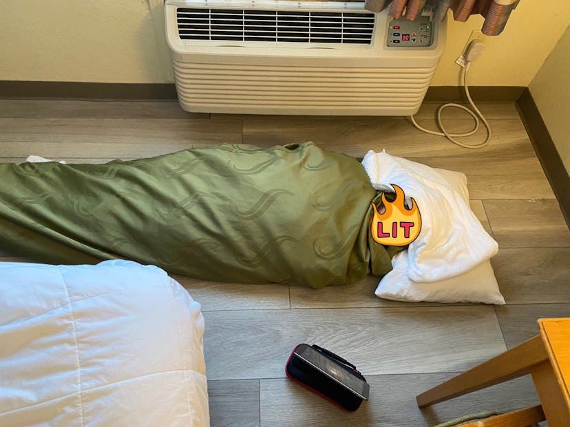 A person laying wrapped in a blanket on the floor with a towel over the head