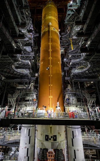 Looking up a giant yellow rocket inside a building. Scaffolding and terraces allow access to the roc...