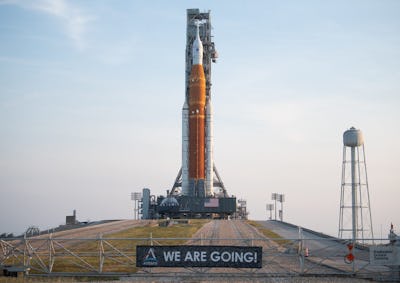 The Space Launch System rocket sits atop a small hill in front of a banner that reads "WE ARE GOING"