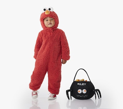 Photo of a kid in a toddler sesame street elmo costume with a monogrammed halloween candy bag next t...