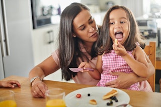 A mom holding her daughter in her lap while she eats pancakes for breakfast.