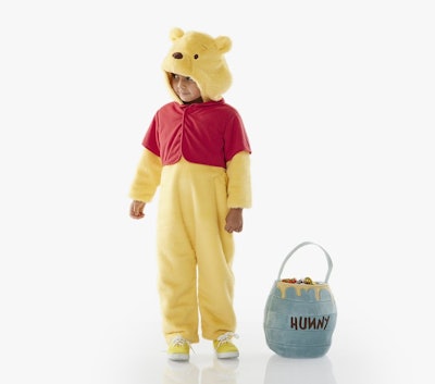 A toddler wearing a winnie the pooh costume standing next to a trick or treat bag in the shape of a ...