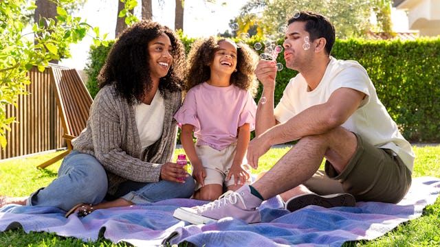 family of three blowing bubbles outside