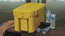 A photo of a yellow cooler sitting outdoors with water bottles next to it.