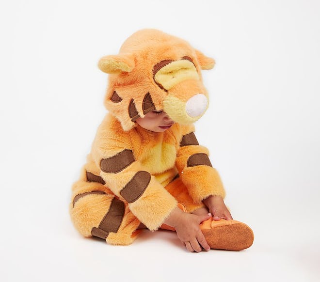 A baby sitting on the ground in an all-white background dressed in a Tigger costume from the pottery...