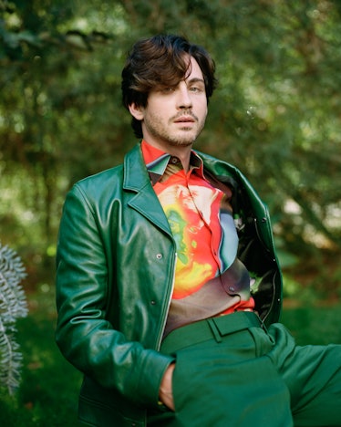 Logan wearing a green Paul Smith jacket, sitting on a chair in a woodsy area.