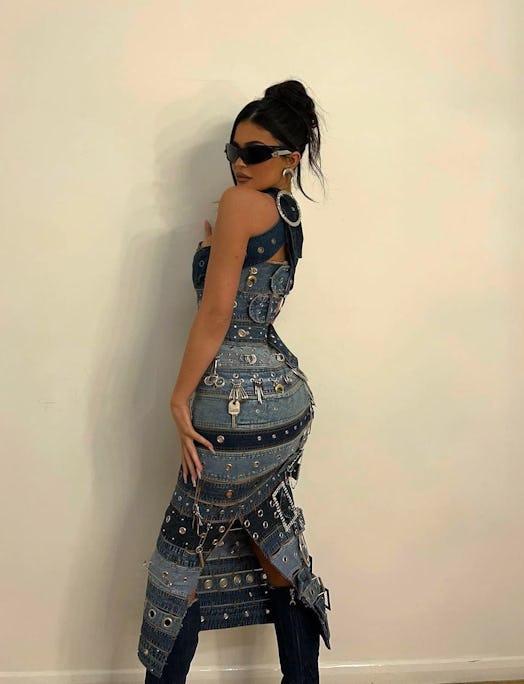 Kylie Jenner posing in a denim dress covered with metal trinkets, straps, keys, and denim heels.