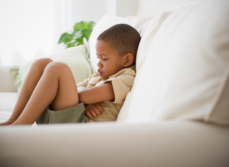 Boy on couch crossing arms and pouting after being disciplined.
