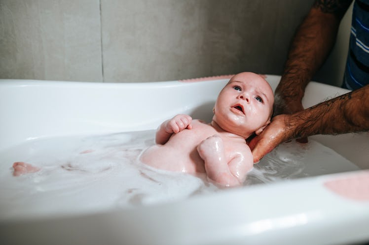 A dad cleaning his baby girl in the bath.