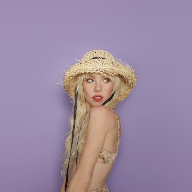 Carly Rae Jepsen wearing a hat and standing in front of a purple background