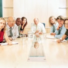 Group of executives at board meeting staring at end of table, judgmentally