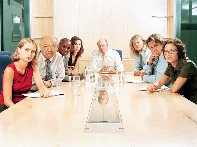 Group of executives at board meeting staring at end of table, judgmentally