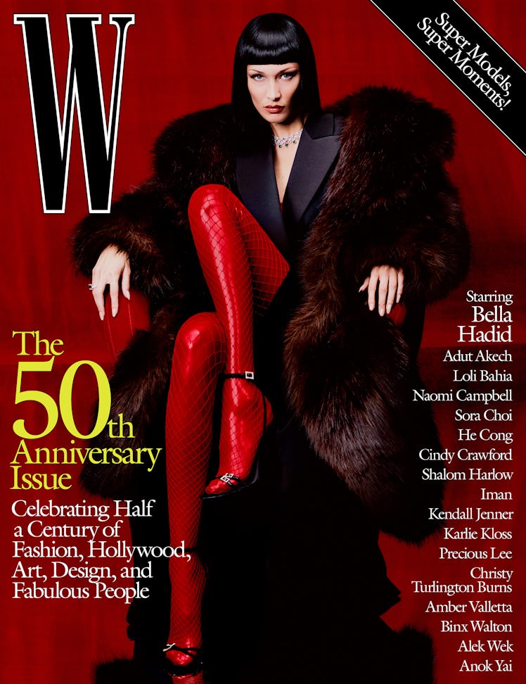 Bella Hadid in a coat, tuxedo dress, sandals, and red fishnets on the cover of W Magazine's 50th ann...