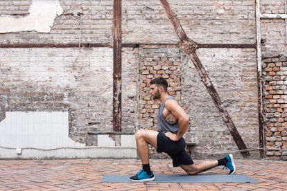 A man does a reverse lunge outside with a background of a brick wall.