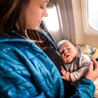 A mother holding her sleeping baby while flying in an airplane.