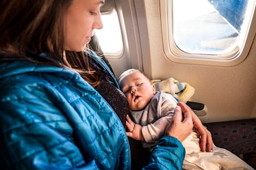 A mother holding her sleeping baby while flying in an airplane.