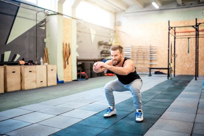 Beweglichkeitsübungen und Dehnübungen für die Knöchel, um agil zu bleiben 1 Ein Mann macht Kniebeugen in einem Fitnessstudio.
