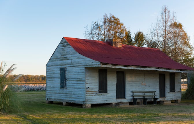 An isolated wooden slave cabin with white walls and a red roof that is being rented on Airbnb