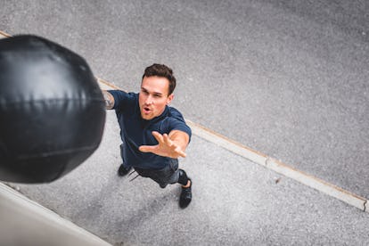 Die besten Kernübungen für Männer, die ein ausgewogenes Körpertraining suchen 5 Ein Mann wirft einen Medizinball gegen eine Wand.