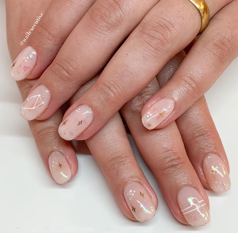 Shimmery nude nails with Libra nail designs in white and gold.