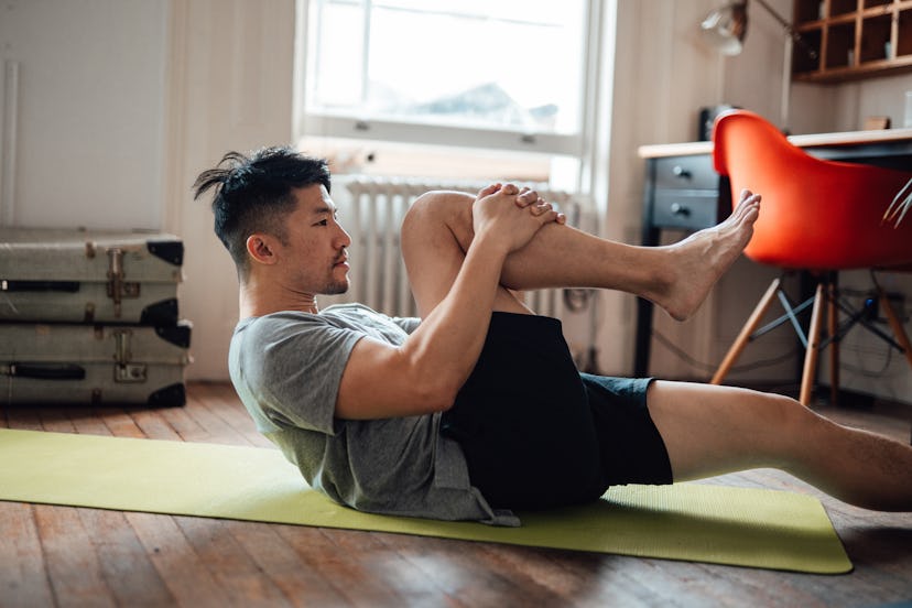 A man lays on a yoga mat and pulls his knee to his chest at home.