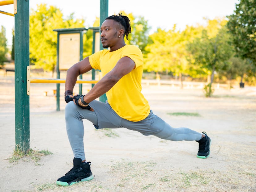 A man leans into a lunge stretch while working out outside at a park.