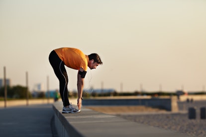 A man on a run bends at the hips to touch his toes.