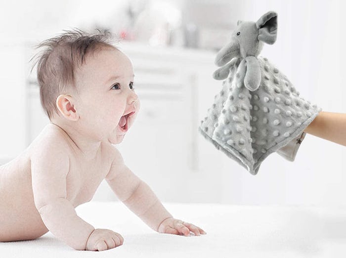 A baby on its tummy with arms holding itself up, smiling at an elephant-themed blanket, which is one...