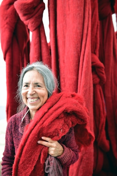 Cecilia Vicuña holding one of her red textile sculptures