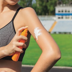 The best sunscreens for runners are must-haves, and in this photo a person in a sports bra applies a...