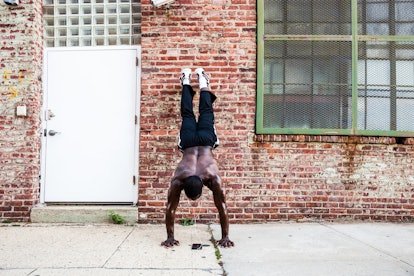 A man doing a wallstand push-up outside in an urban area.