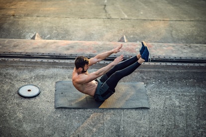 A man does a v sit-up outdoors on cement on a yoga mat.