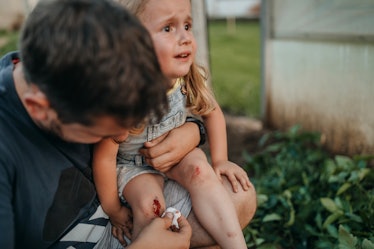 A dad cleans up a scrape on his distressed daughter's knee.