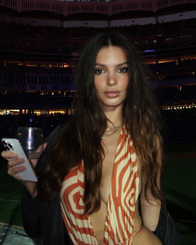 Emily Ratajkowski wearing a deep plunging bathing suit and mini skirt to Bad Bunny's concert at Yank...