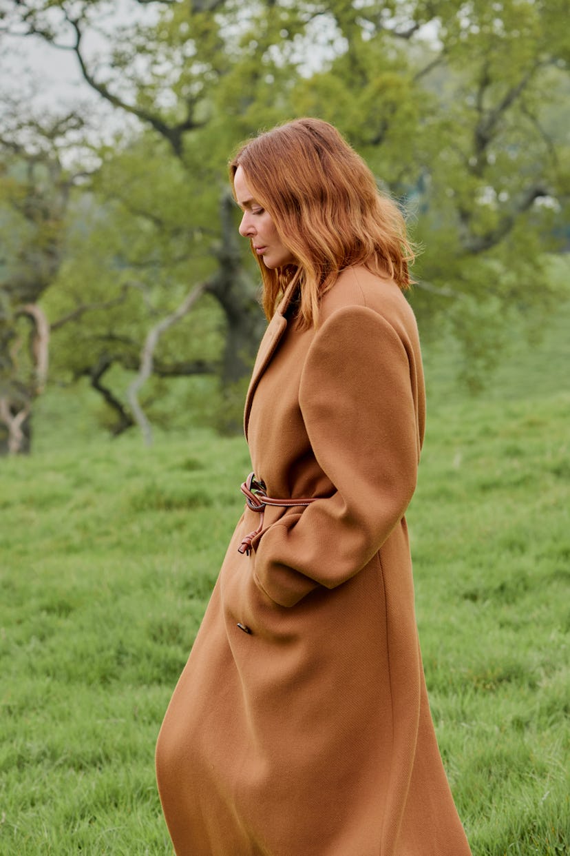 Stella McCartney walking through the forest in a camel colored coat