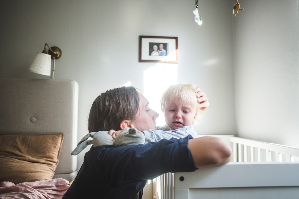A dad hugging his child who is standing in a crib.