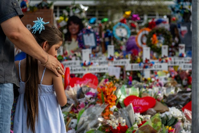Little girl standing in front of a wall of flowers, a tribute to victims of gun violence