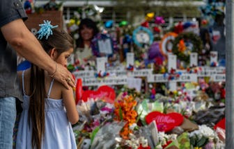 Little girl standing in front of a wall of flowers, a tribute to victims of gun violence