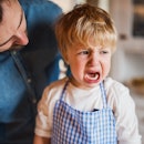 A child in an apron crying as his dad leans over him.