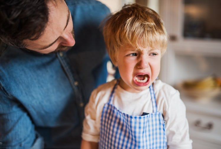 A child in an apron crying as his dad leans over him.