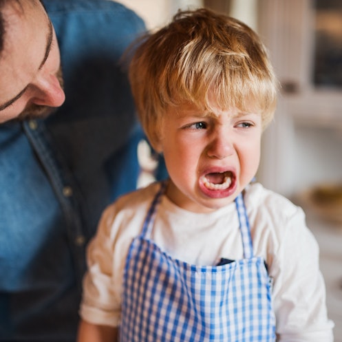 A child in an apron crying as his dad leans over him.