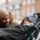 A dad in winter checks on his baby in a stroller.