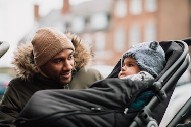 A dad in winter checks on his baby in a stroller.