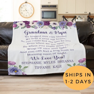 White blanket with purple flowers and purple script with a note to grandma and papa from the kids an...