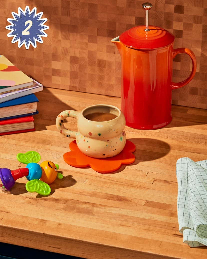 Kitchen countertop with an orange teapot closest to the wall, a white mug with polka dots on an oran...
