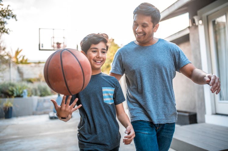 A confident boy spins a basketball while walking with his dad.