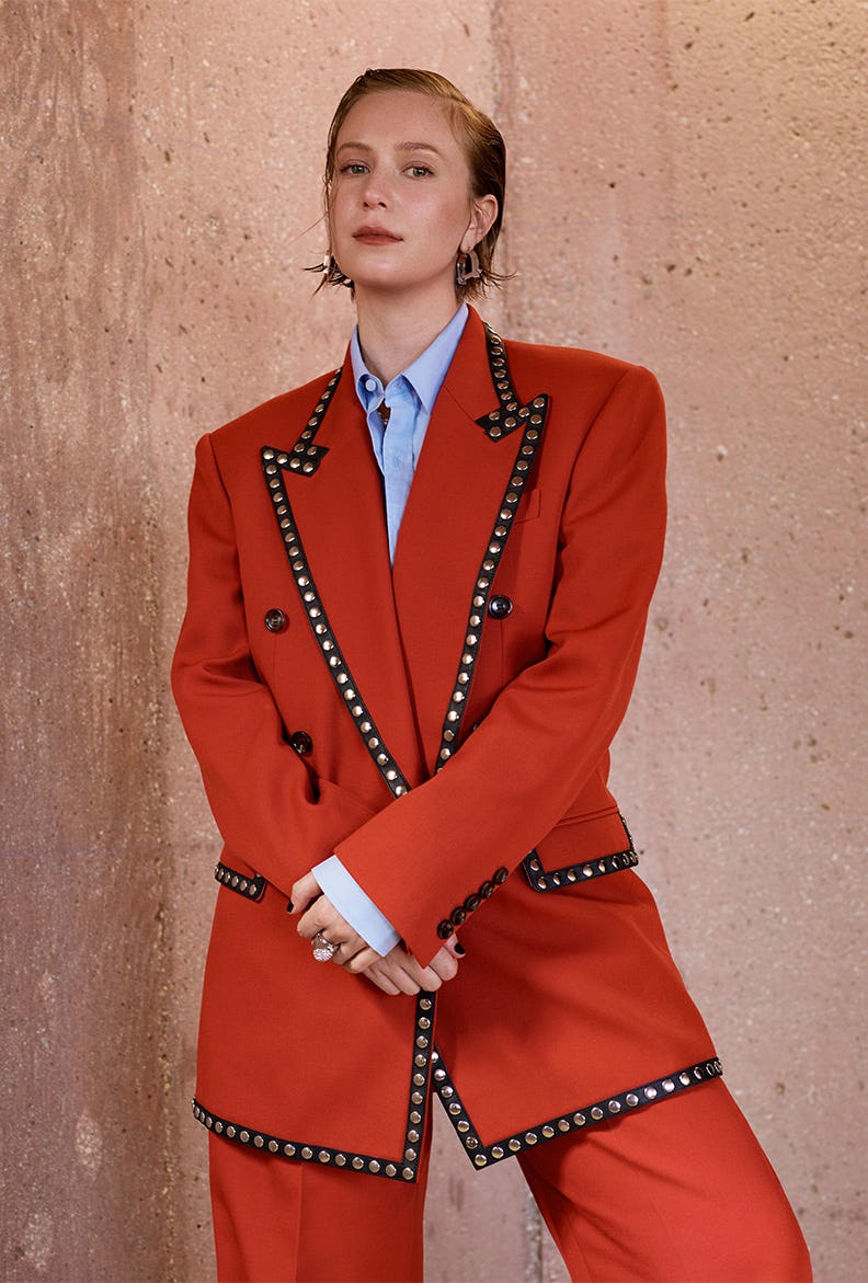 Hannah Einbinder posing in a red suit with silver studs and a blue button-up shirt