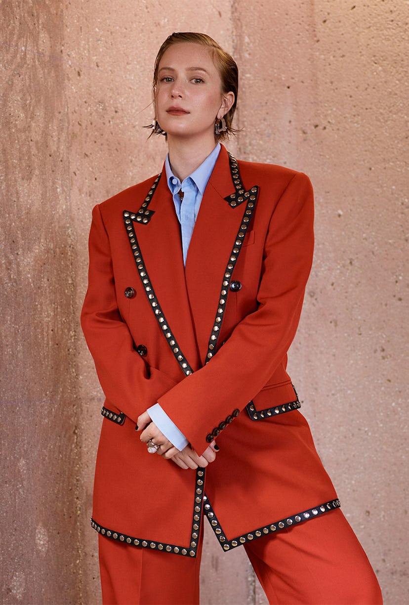 Hannah Einbinder posing in a red suit with silver studs and a blue button-up shirt